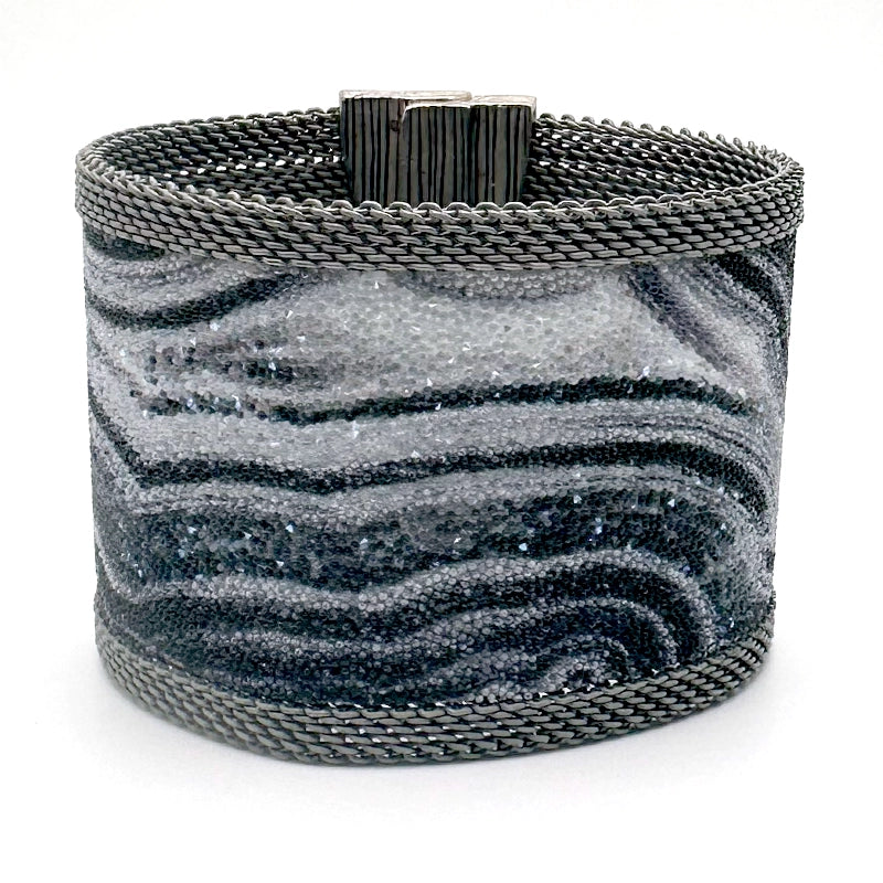 Wide cuff bracelet with black and white agate slice pattern highlighted by shiny and matte Swarovski micro-crystals, with matte silver mesh edges, tilted to show closed magnetic clasp, on a white background.