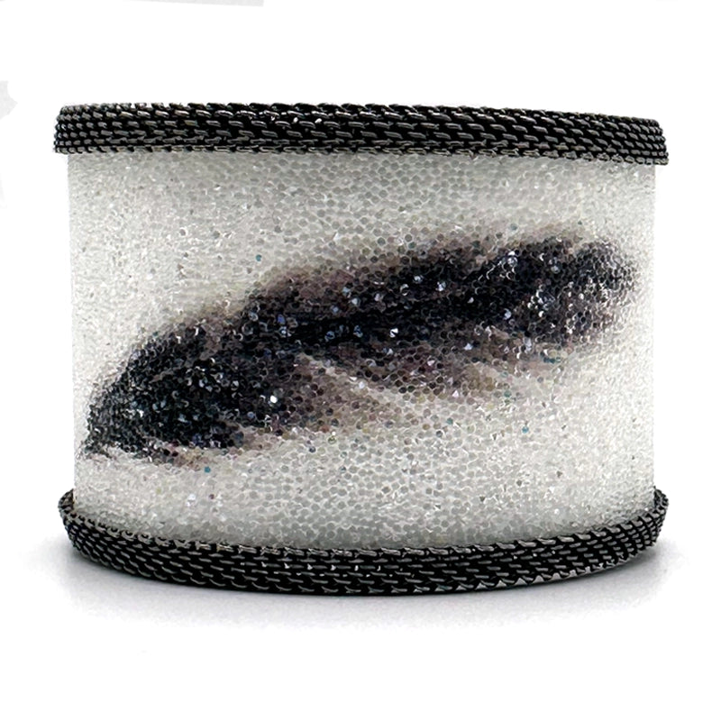 Wide cuff bracelet with white Swarovski micro-crystals surrounding a shimmery black crystal feather image, with gunmetal mesh edges, on a white background.