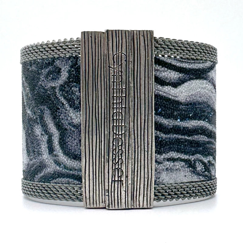 Back view of a wide cuff bracelet with black and white agate slice pattern highlighted by shiny and matte Swarovski micro-crystals, with matte silver mesh edges, showing off the closed signature Cynthia Desser magnetic clasp, on a white background.