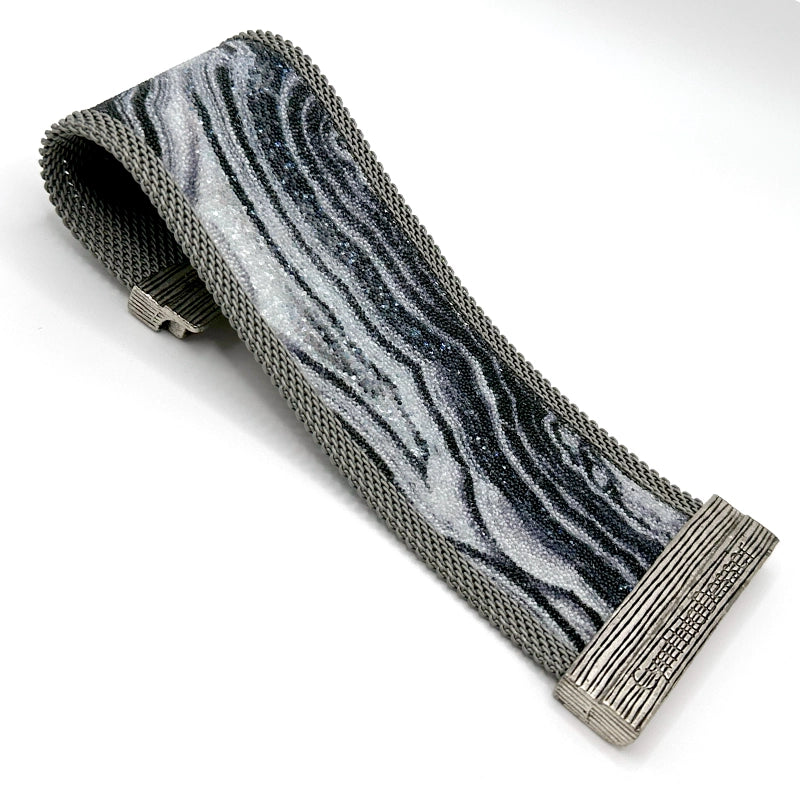 Wide cuff bracelet with black and white agate slice pattern highlighted by shiny and matte Swarovski micro-crystals, with matte silver mesh edges, open with one end curled under to show off the signature Cynthia Desser magnetic clasp, on a white background.