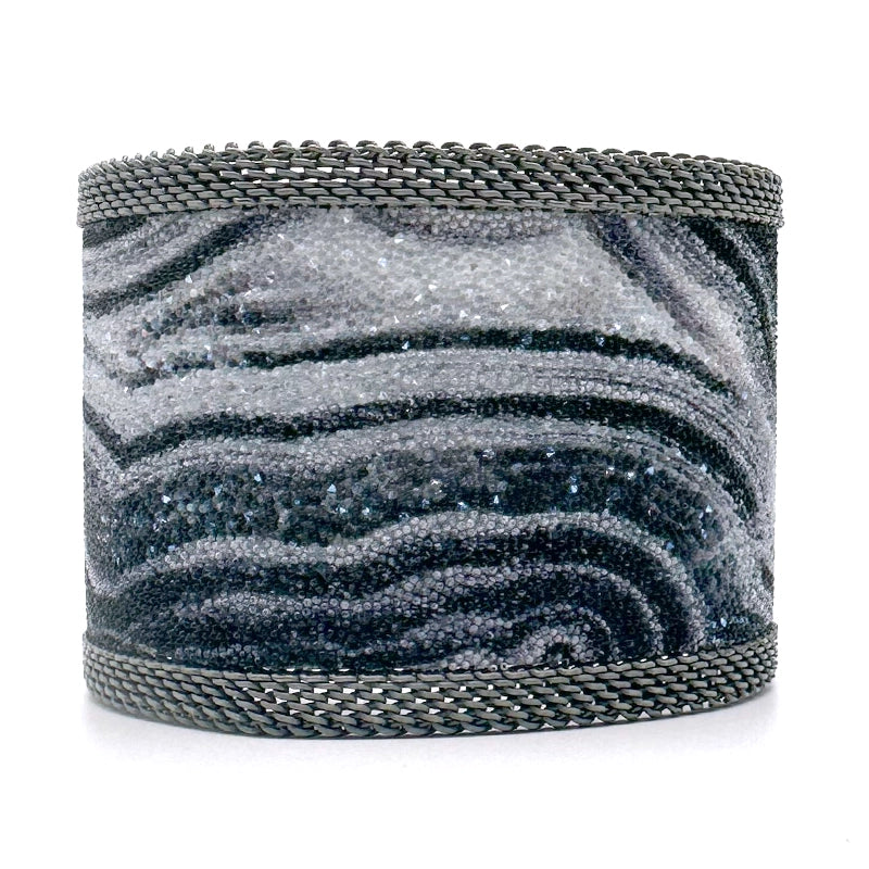 Wide cuff bracelet with black and white agate slice pattern highlighted by shiny and matte Swarovski micro-crystals, with matte silver mesh edges, on a white background.