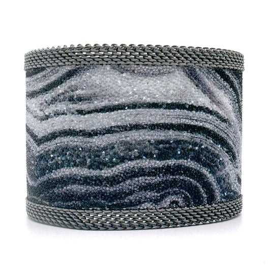 Wide cuff bracelet with black and white agate slice pattern highlighted by shiny and matte Swarovski micro-crystals, with matte silver mesh edges, on a white background.
