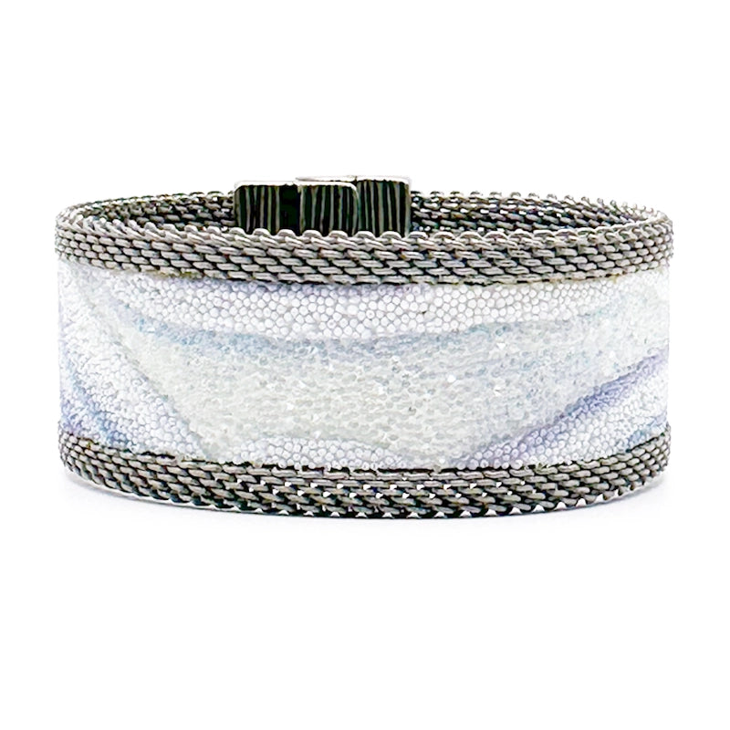 Narrow cuff bracelet with blue lace agate slice pattern highlighted by shiny and matte Swarovski micro-crystals, with matte silver mesh edges, on a white background.