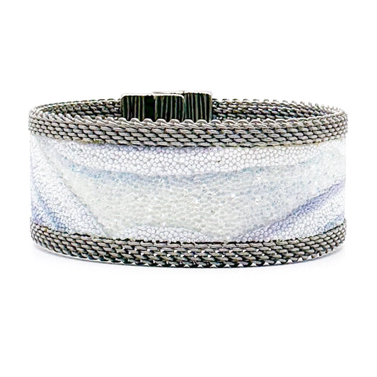 Narrow cuff bracelet with blue lace agate slice pattern highlighted by shiny and matte Swarovski micro-crystals, with matte silver mesh edges, on a white background.