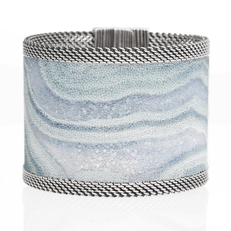 Wide cuff bracelet with blue lace agate slice pattern highlighted by shiny and matte Swarovski micro-crystals, with silver mesh edges, tilted to show closed magnetic clasp, on a white background.