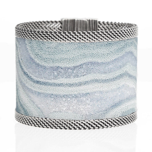 Wide cuff bracelet with blue lace agate slice pattern highlighted by shiny and matte Swarovski micro-crystals, with silver mesh edges, tilted to show closed magnetic clasp, on a white background.