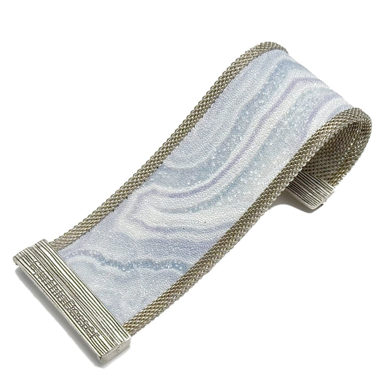 Wide cuff bracelet with blue lace agate slice pattern highlighted by shiny and matte Swarovski micro-crystals, with silver mesh edges, open with one end curled under to show off the signature Cynthia Desser magnetic clasp, on a white background.