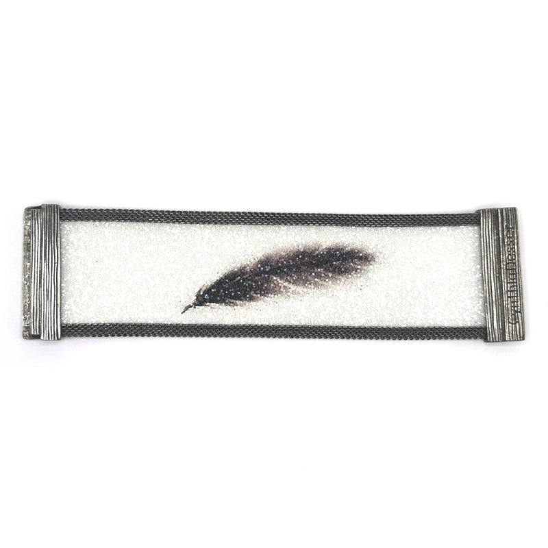 Wide cuff bracelet with white Swarovski micro-crystals surrounding a shimmery black crystal feather image, with gunmetal mesh edges, laid open flat to show the signature Cynthia Desser magnetic clasps, on a white background.