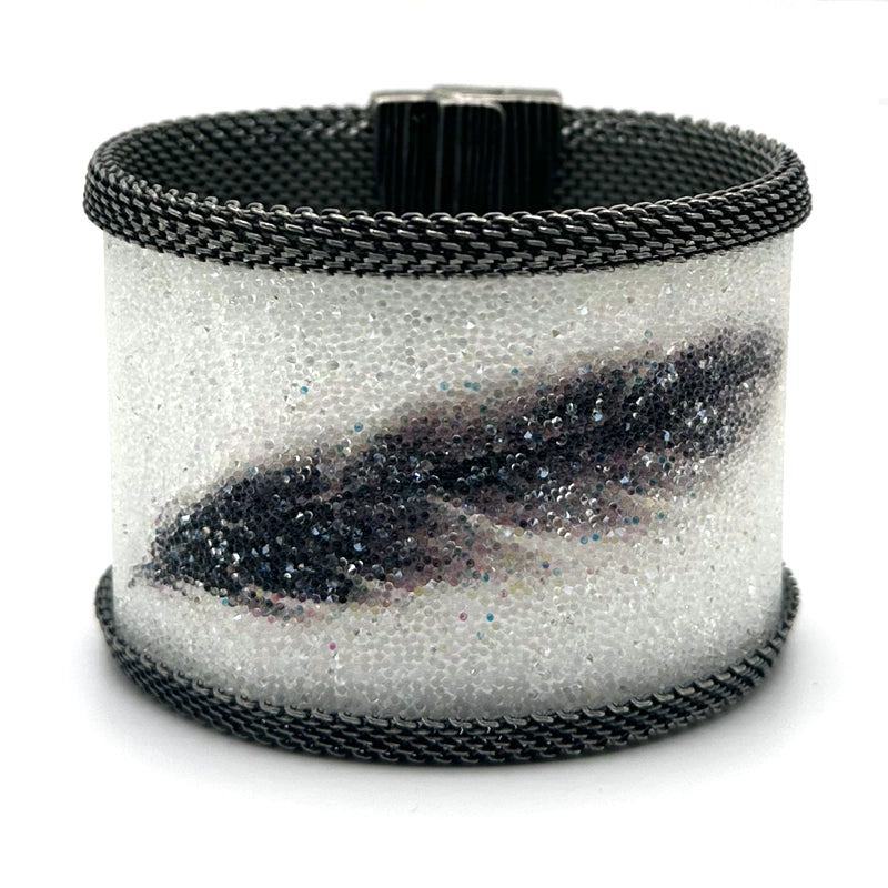 Wide cuff bracelet with white Swarovski micro-crystals surrounding a shimmery black crystal feather image, with gunmetal mesh edges, tilted to show the closed magnetic clasp, on a white background.