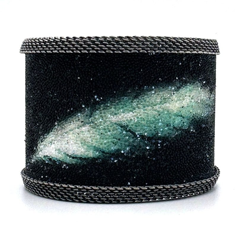 Wide cuff bracelet with matte black Swarovski micro-crystals surrounding a shimmery green and white crystal feather image, with oxidized silver mesh edges, on a white background.