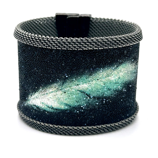 Wide cuff bracelet with matte black Swarovski micro-crystals surrounding a shimmery green and white crystal feather image, with oxidized silver mesh edges, tilted to show the closed magnetic clasp, on a white background.
