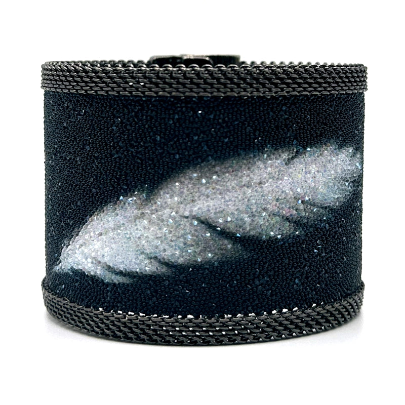 Wide cuff bracelet with matte black Swarovski micro-crystals surrounding a shimmery white crystal feather image, with gunmetal mesh edges, on a white background.