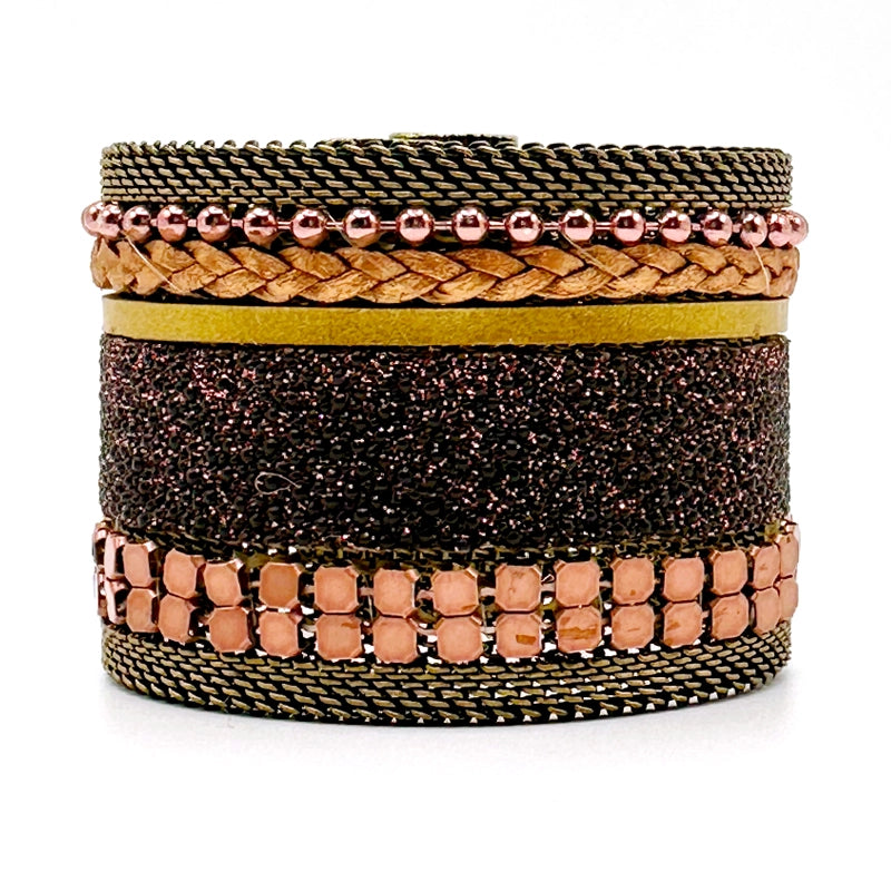 Wide cuff bracelet with a mix of copper colored metal elements, metallic gold leather braids or strips, and pink-brown shimmery stingray, with brass mesh edges, on a white background.
