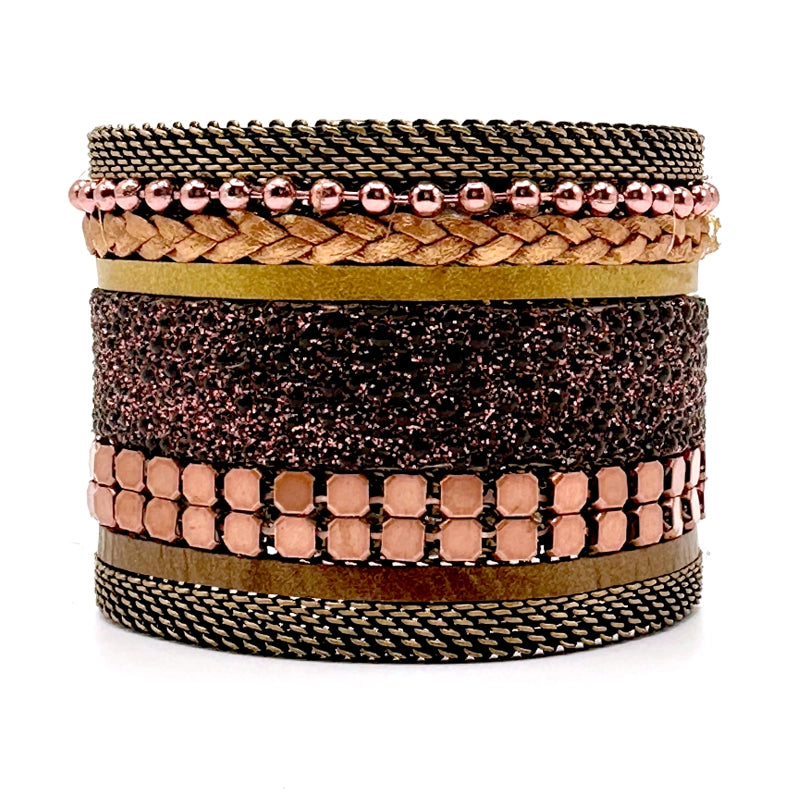 Wide cuff bracelet with a mix of copper colored metal elements, metallic gold leather braids or strips, and pink-brown shimmery stingray, with brass mesh edges, on a white background.