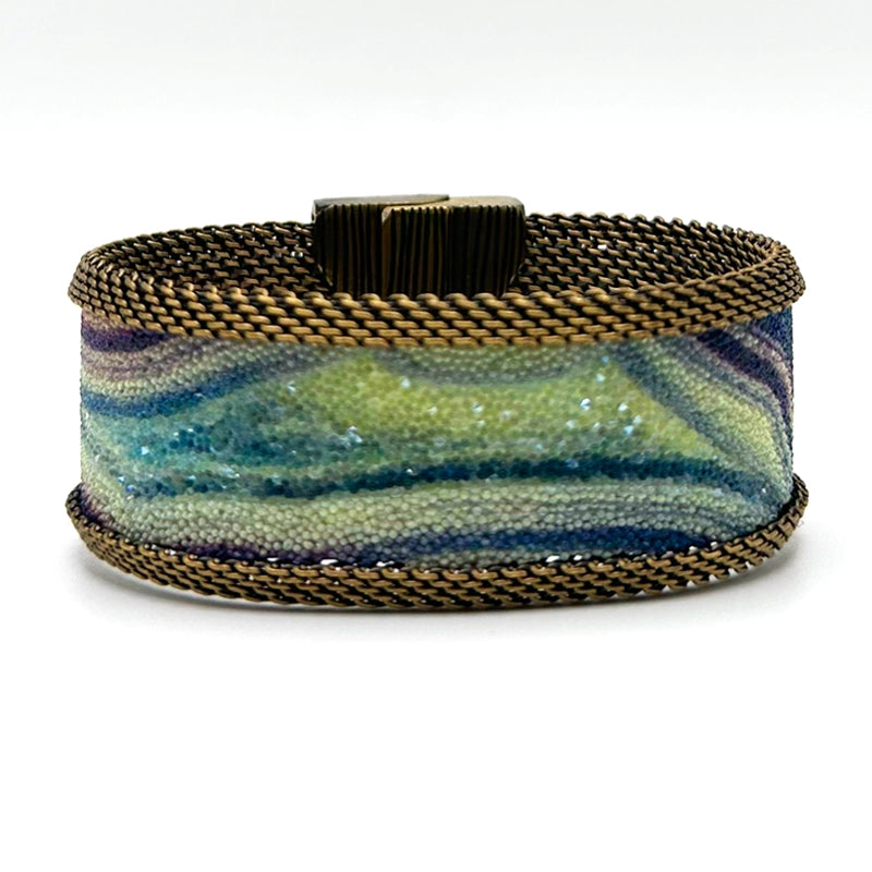 Narrow cuff bracelet with green-blue multi-color agate slice pattern highlighted by shiny and matte Swarovski micro-crystals, with brass mesh edges, on a white background.