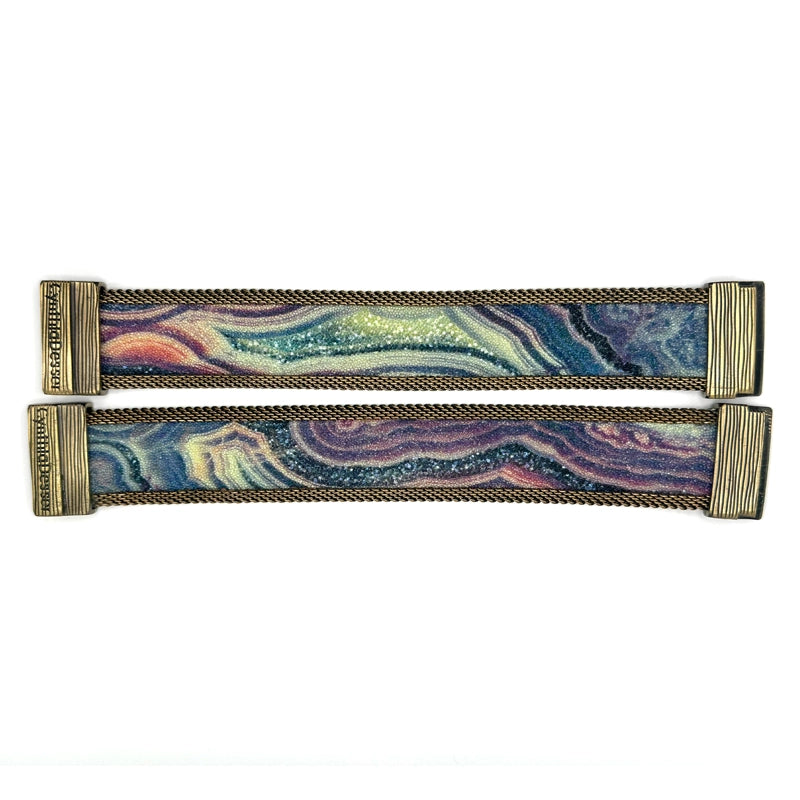 Two narrow cuff bracelets with multi-color agate slice patterns highlighted by shiny and matte Swarovski micro-crystals, with brass mesh edges, laid open flat to show the signature Cynthia Desser magnetic clasps, on a white background.